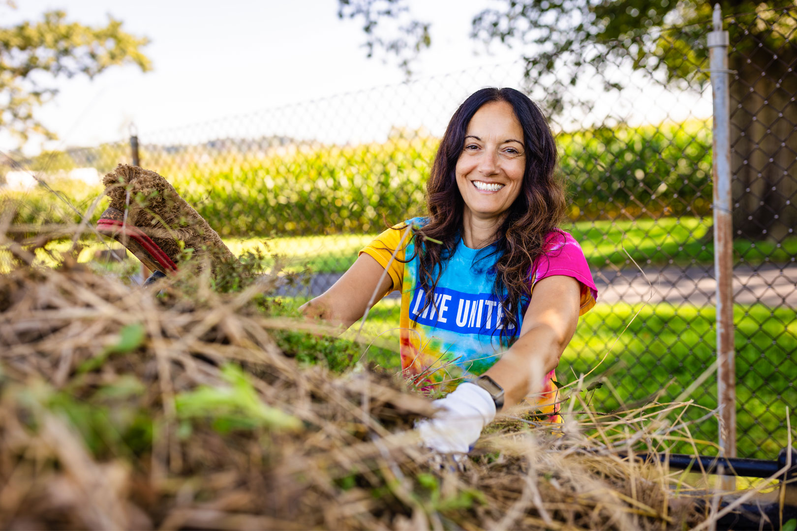 Volunteer wearing gloves works outdoors moving yard debris during a community service project.